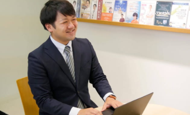 スーツを着た男性がPCを開いて笑顔で座っている様子